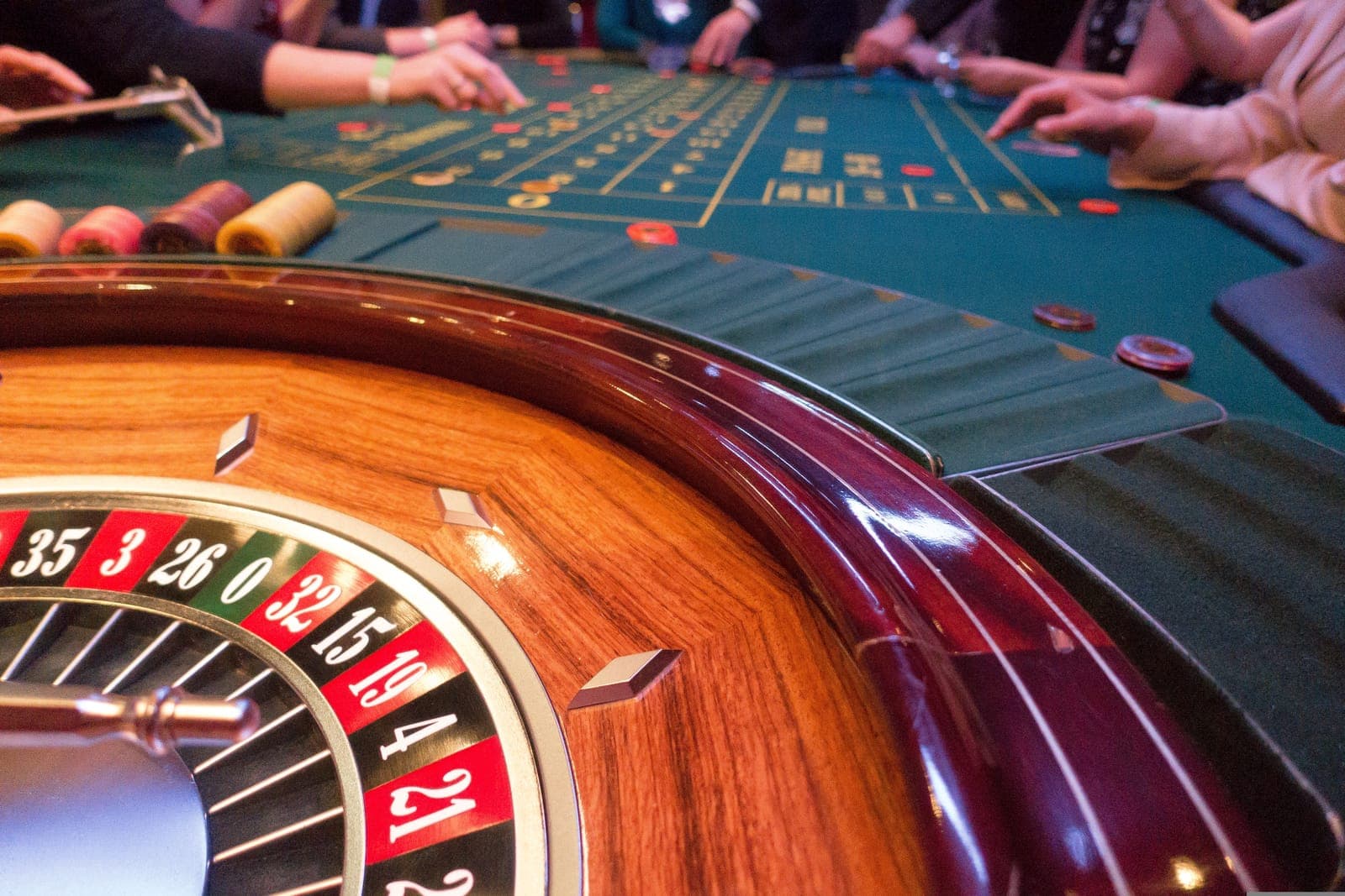 Close-up of a roulette wheel beside a green felt table with players placing chips
